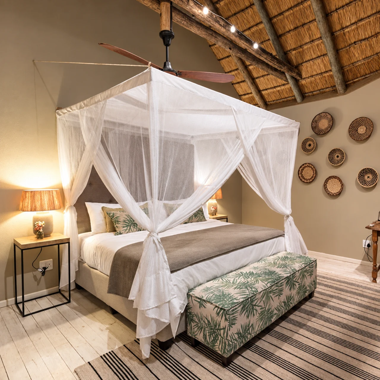 A suspended white mosquito net above a bed under a thatched lodge roof.