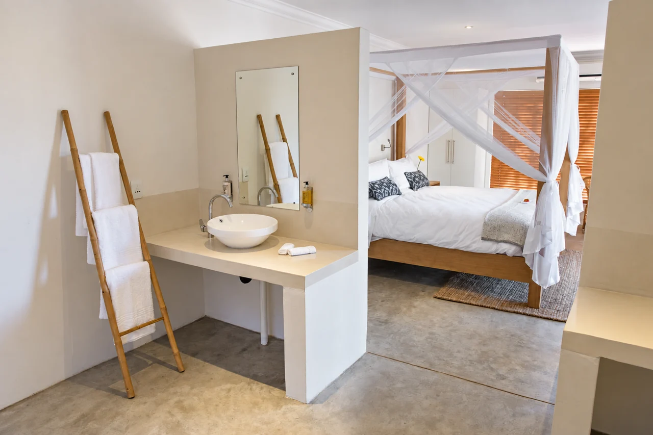 An airy bedroom with a white mosquito net, seen from the bathroom.
