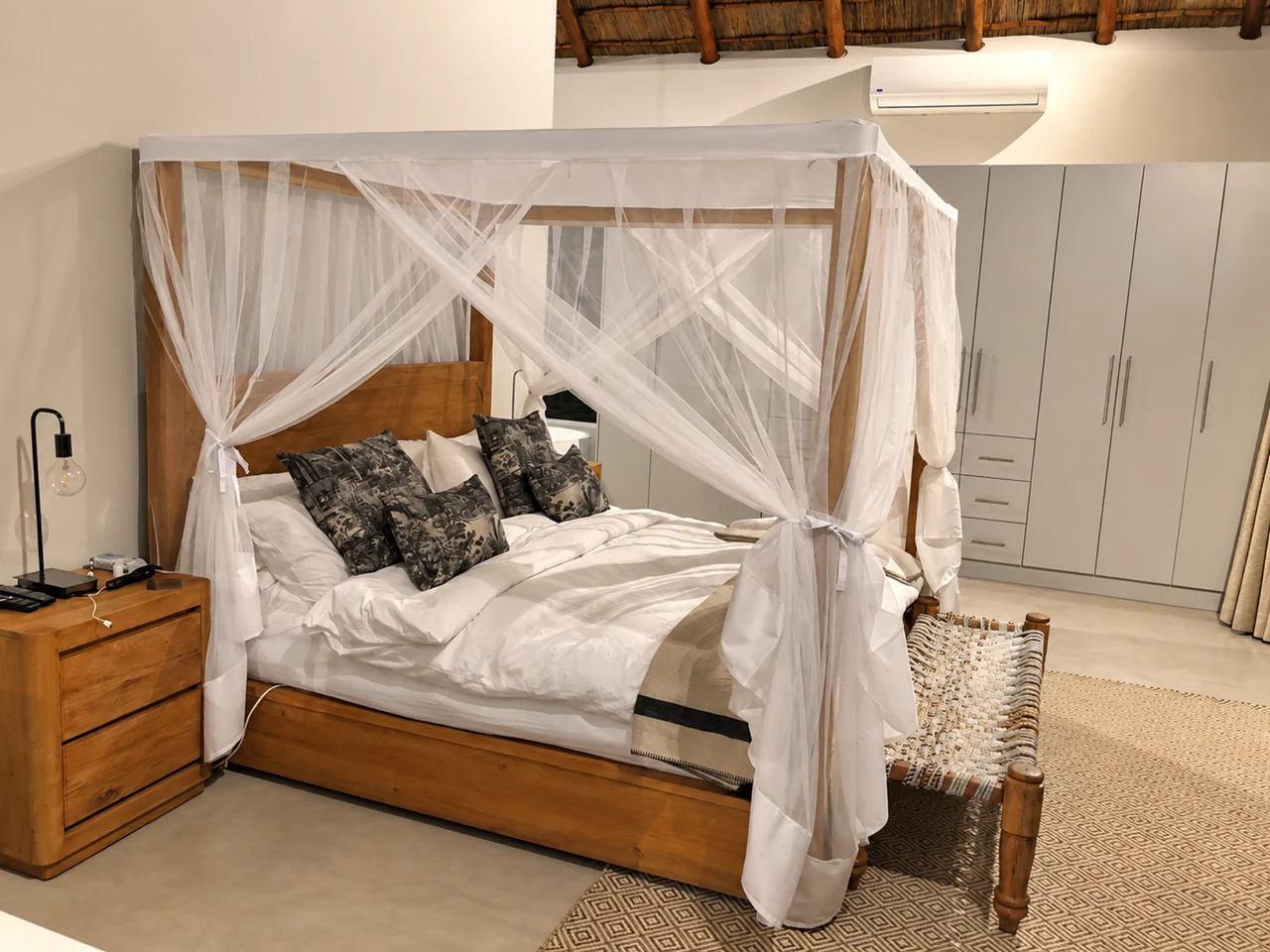 A timber bed frame draped in white netting in a warmly lit room.